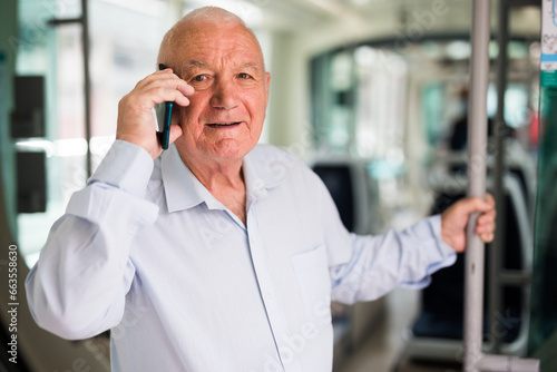 Old European man standing in streetcar and having telephone conversation. © JackF