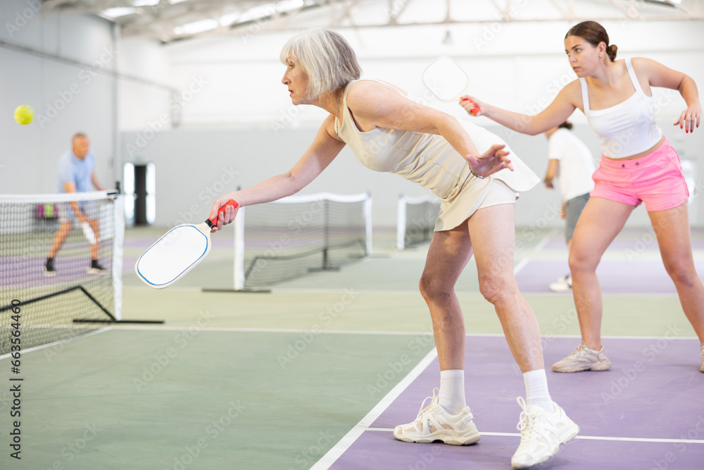 Mature adult woman playing doubles pickleball game, healthy lifestyle concept