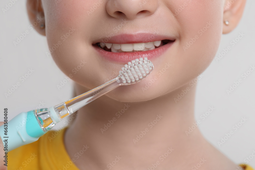 Girl brushing her teeth with electric toothbrush on light grey background, closeup Girl brushing her teeth with electric toothbrush on light grey background, closeup