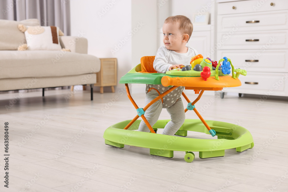 Cute little boy making first steps with baby walker at home, space for text Cute little boy making first steps with baby walker at home, space for text