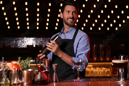 Bartender with shaker preparing fresh alcoholic cocktail in bar
