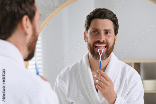 Canvas Print Handsome man brushing his tongue with cleaner near mirror in bathroom