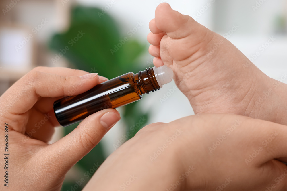 Mother applying essential oil from roller bottle onto her baby`s heel on blurred background, closeup Mother applying essential oil from roller bottle onto her baby`s heel on blurred background, closeup