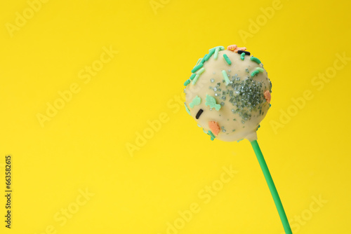 Delicious confectionery. Sweet cake pop decorated with sprinkles on yellow background  closeup. Space for text