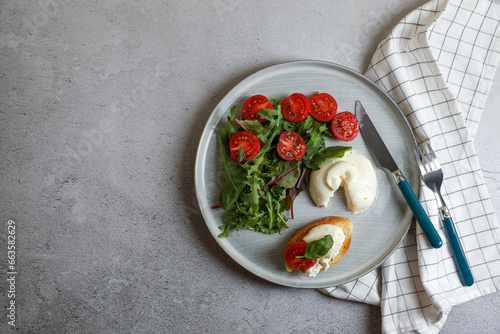 Delicious burrata cheese with tomatoes, arugula and toast served on grey table, top view. Space for text