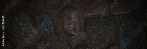 Ground texture with large stones. Old pavement of granite boulders. Stone decoration of sidewalks and pedestrian walkways. Dark wide panoramic background for design.