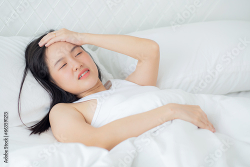 Young asian woman lying on bed pain headache in the bedroom at home, unhappy female exhaustion and sick headache, anxiety and unwell, dizziness and disorder, medical and health concept.