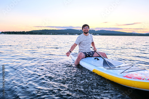 A man sits on a paddle board at sunset.
