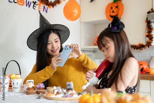 A kind Asian mom enjoys making Halloween cupcakes with her young daughter in the kitchen.