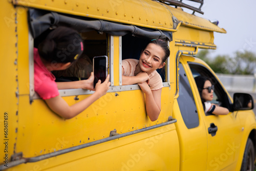 teenager girl friends sitting in yellow a minibus, and use smartphone to take pictyres of them chiamg mai thailand, amazing travel tourist in the rain season concept, photo