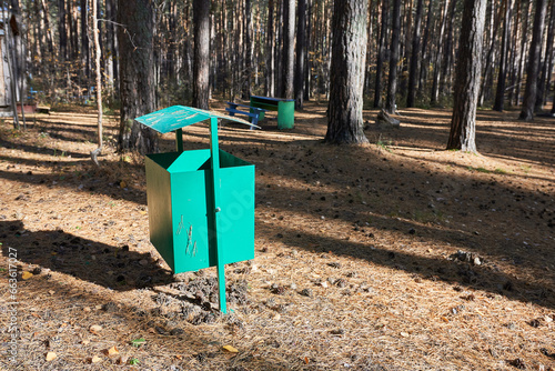 A green trash can in a pine forest.