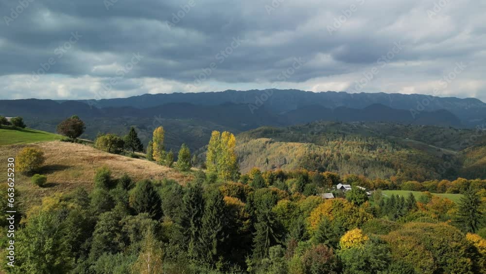 Aerial rural landscape with autumn forest in mountains. Fall season. Scenic autumn foliage in vibrant yellow, orange and green leaves on top of trees. National Park Piatra Craiului on background Aerial rural landscape with autumn forest in mountains. Fall season. Scenic autumn foliage in vibrant yellow, orange and green leaves on top of trees. National Park Piatra Craiului on background