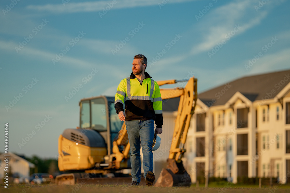 Builder in a construction site. Builder with excavator ready to build new house. Construction builder wear building uniform on excavation truck digging, builder with buildings construction background. Builder in a construction site. Builder with excavator ready to build new house. Construction builder wear building uniform on excavation truck digging, builder with buildings construction background.