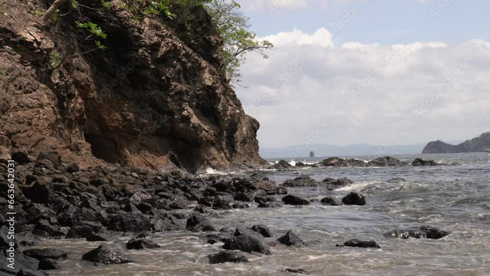 Ocean waves crashing on rocky shores of Playa Penca as fishing boat drives in background, Costa Rica Ocean waves crashing on rocky shores of Playa Penca as fishing boat drives in background, Costa Rica