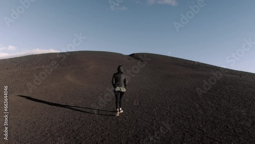 Wide gimbal shot of young petite woman walking up hill at craters of the moon in Idaho photo