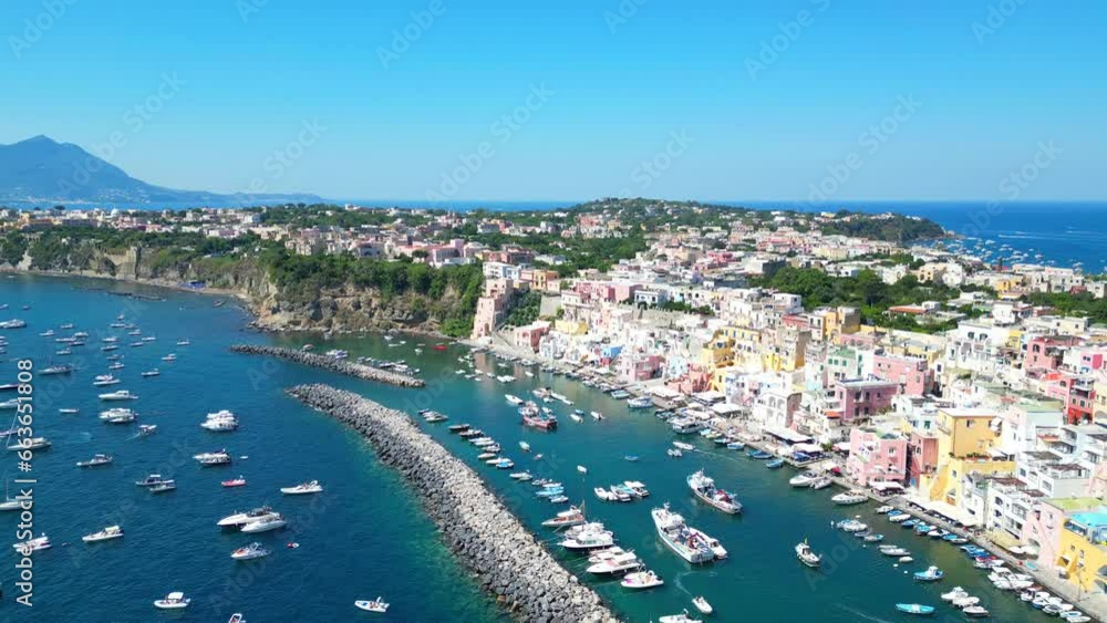 Establishing aerial push-in shot from Panoramica sulla Corricella on Procida Island (Isola di Procida) with breakwaters, boats on the Tyrrhenian Sea, pastel buildings, greenery, Naples' gulf, Vesuvius Establishing aerial push-in shot from Panoramica sulla Corricella on Procida Island (Isola di Procida) with breakwaters, boats on the Tyrrhenian Sea, pastel buildings, greenery, Naples' gulf, Vesuvius