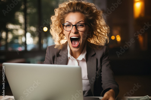Happy young businesswoman celebrating achievement or online success while looking at laptop screen.