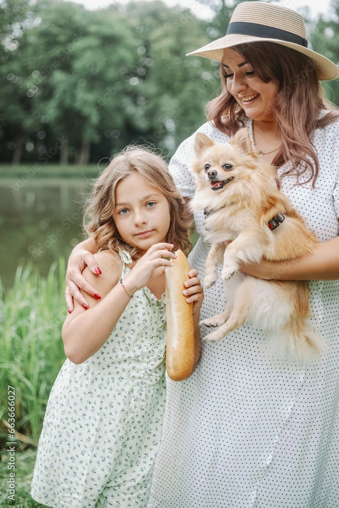 Mother's love. Charming mom,daughter in summer dresses, with dog in their arms in nature on summer. 