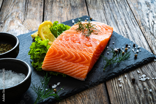 Fresh raw salmon steak with salt and fresh vegetables on wooden background 