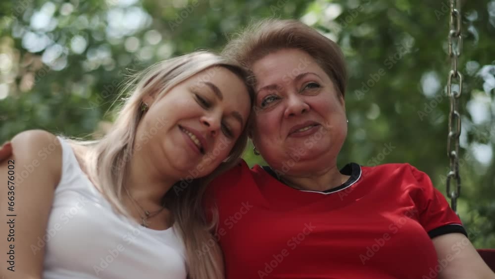 An adult mother with a young daughter swinging on a swing in the garden next to her house. Hugging, talking and laughing. An adult mother with a young daughter swinging on a swing in the garden next to her house. Hugging, talking and laughing.