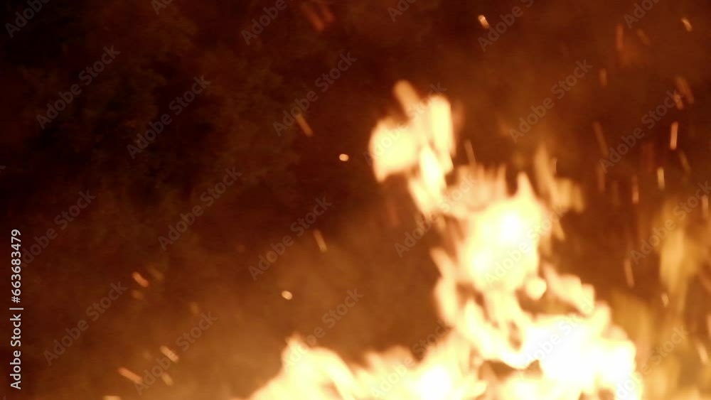 Intentional light blur: within the serene night, blazing, fervent flames burst forth from a crackling bonfire, with fascinating sparks fiying away. Captured in slow-motion.