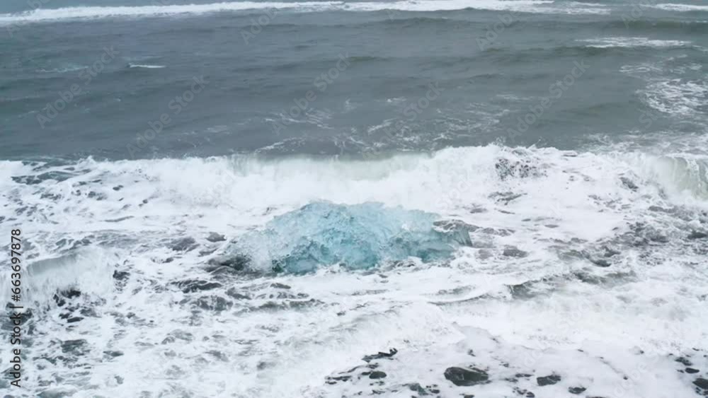 Stunning drone shot of waves breaking on a beautiful ice rock at Diamond Beach in Iceland (slow motion) Stunning drone shot of waves breaking on a beautiful ice rock at Diamond Beach in Iceland (slow motion)