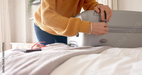 Caucasian woman packing and zipping suitcase on bed at home, copy space, slow motion photo