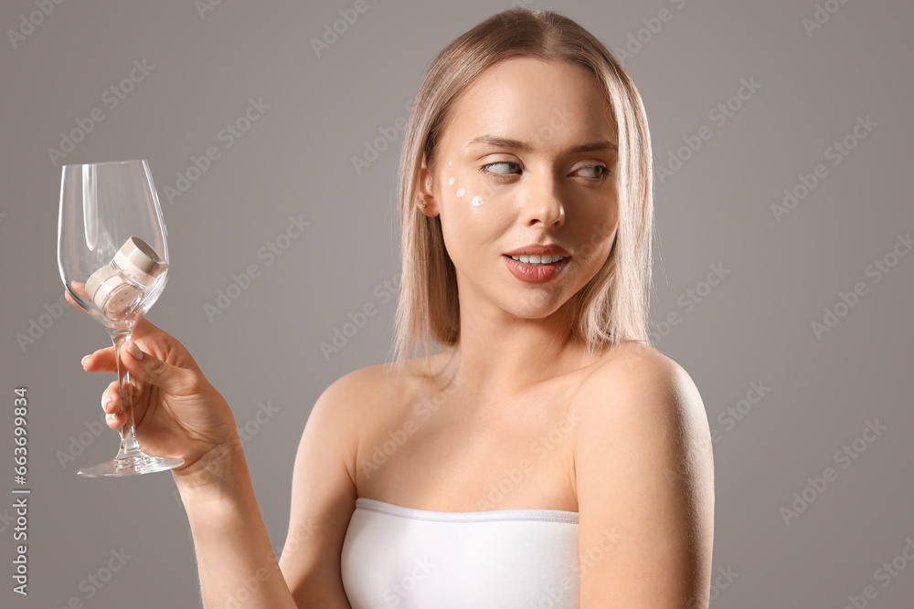 Sexy young woman with glass and facial creams on grey background Sexy young woman with glass and facial creams on grey background