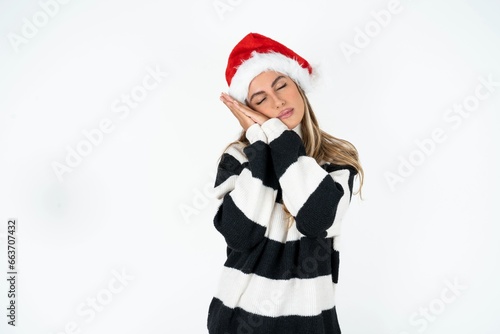Beautiful hispanic woman wearing christmas hat and striped knitted sweater sleeping tired dreaming and posing with hands together while smiling with closed eyes.