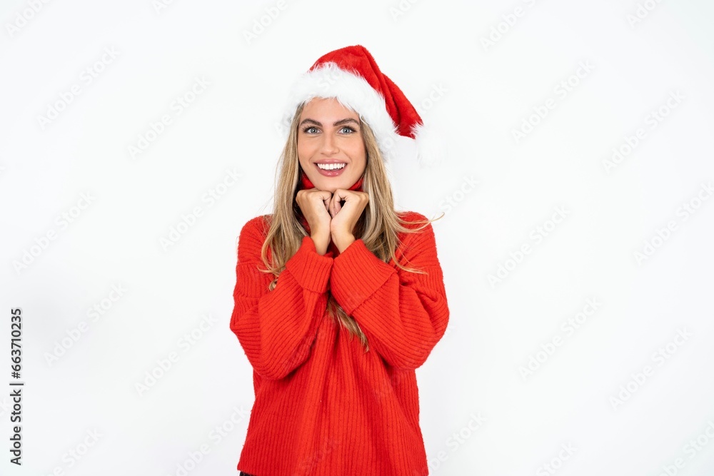 Satisfied Beautiful hispanic woman wearing christmas hat and red knitted sweater touches chin with both hands, smiles pleasantly, rejoices good day with lover Satisfied Beautiful hispanic woman wearing christmas hat and red knitted sweater touches chin with both hands, smiles pleasantly, rejoices good day with lover