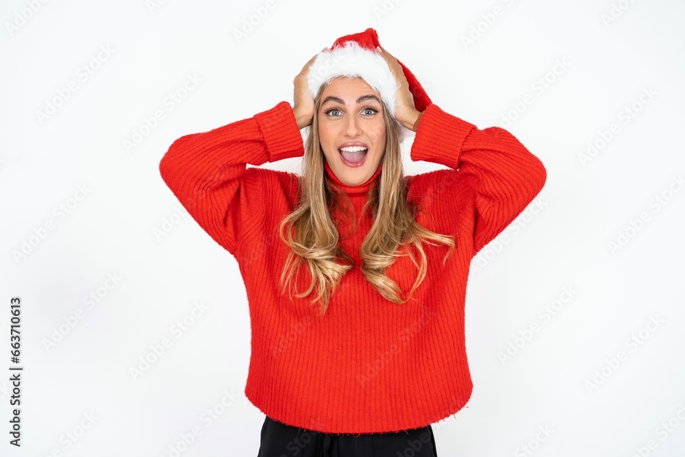 Φωτογραφία Cheerful overjoyed Beautiful hispanic woman wearing christmas hat and red knitted sweater reacts rising hands over head after receiving great news