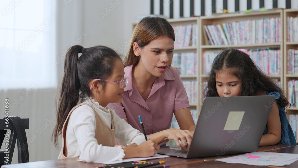 Young women elementary teacher and two little girl pupil in classroom. Teacher and students using laptop for learning lesson for success. Back to school Young women elementary teacher and two little girl pupil in classroom. Teacher and students using laptop for learning lesson for success. Back to school