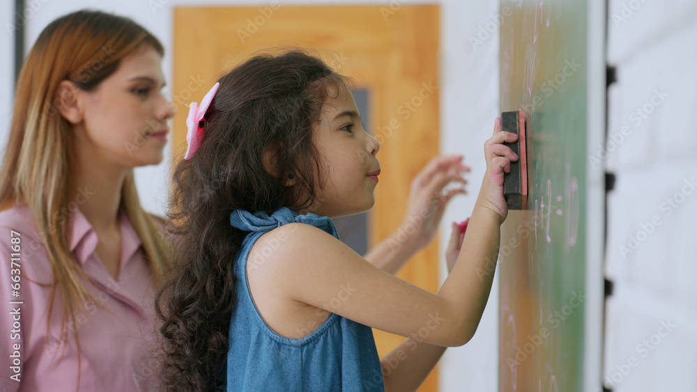 Schoolgirl standing by the board and wiping chalkboard. Kindergarten Asian cute little girl wiping clean or erase chalk on green school board. Back to School. Education concept Schoolgirl standing by the board and wiping chalkboard. Kindergarten Asian cute little girl wiping clean or erase chalk on green school board. Back to School. Education concept