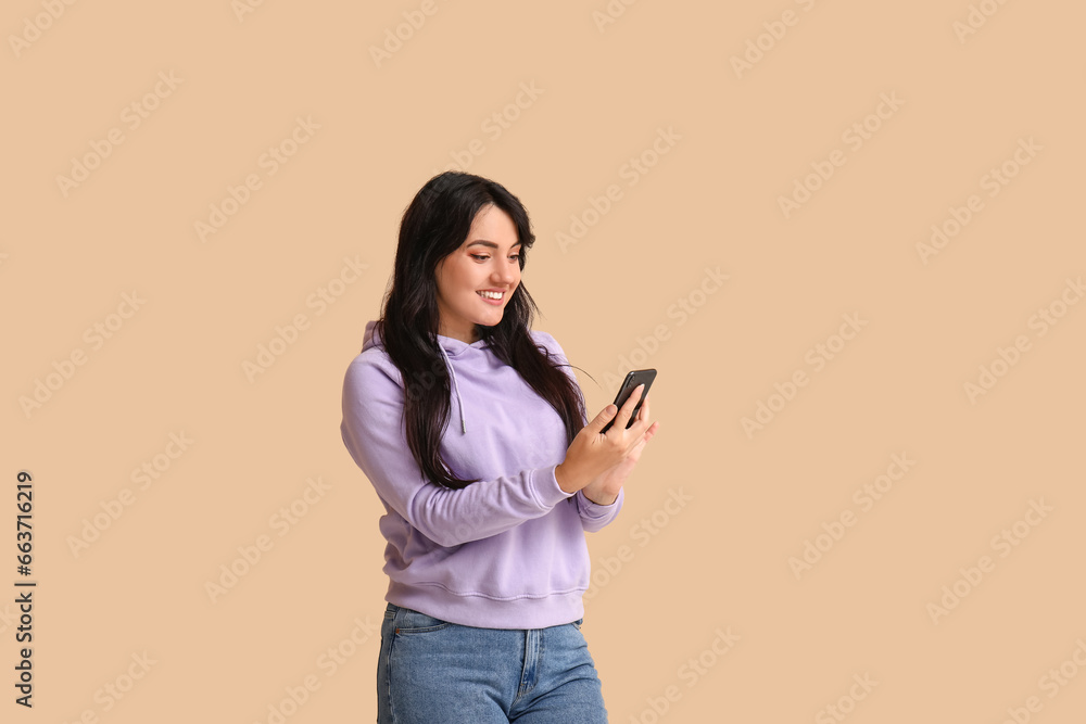 Portrait of happy young brunette with smartphone on beige background