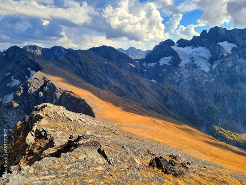 Snow-Capped Mountains with Green and Dry Grass, Clouds, and a Stunning Sky
