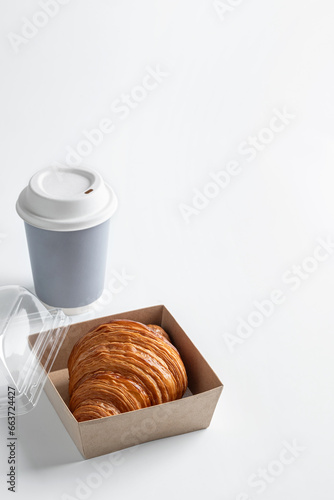 Delicious croissant in an open lunch box with a glass of coffee on a white background. Takeaway baking