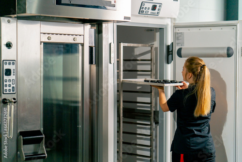 Shot from the back of a girl a pastry chef puts candy to harden in the refrigerator and sets cooling temperature