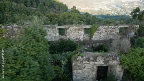 Aerial pan across broken walls of monastery overgrown with vines in the forest of Galicia Spain photo