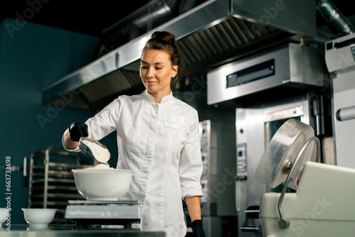 Obraz na plátne A female baker in  white chef's tunic kneads dough to prepare and bake bread in