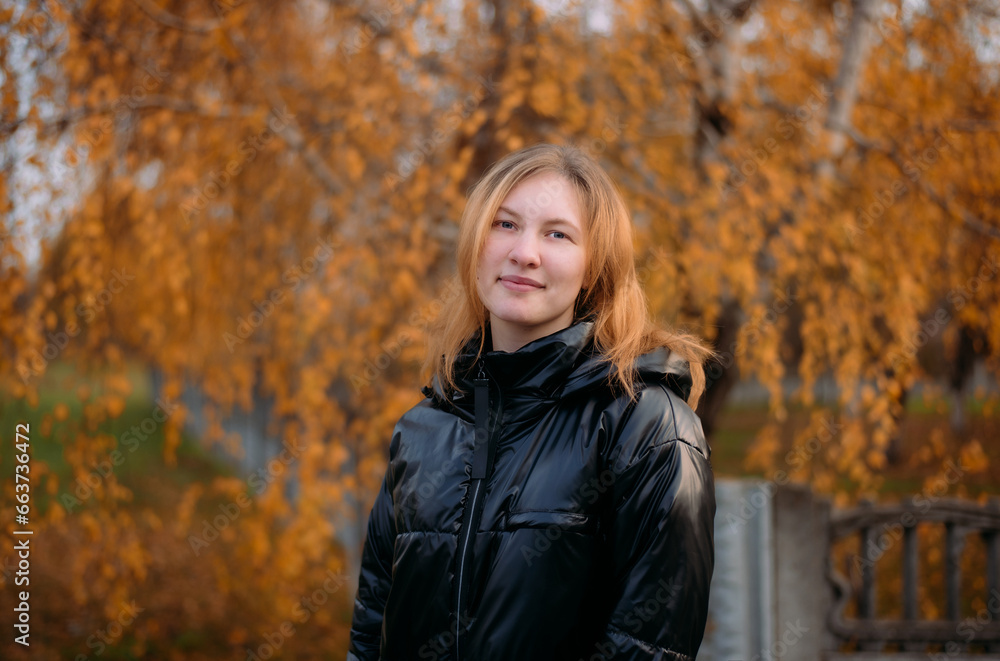 Portrait of a beautiful girl in a dark jacket standing near colorful autumn leaves. A young woman relaxes in a park against the background of yellow trees in the autumn season. Portrait of a beautiful girl in a dark jacket standing near colorful autumn leaves. A young woman relaxes in a park against the background of yellow trees in the autumn season.