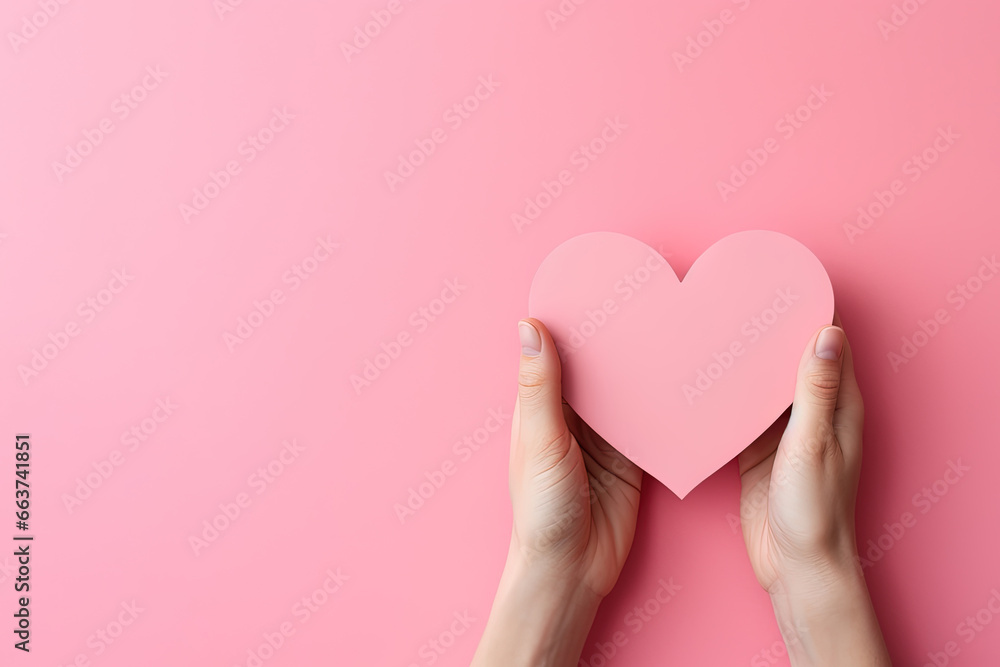 hand holds a heart love shape on a pink background with copy space