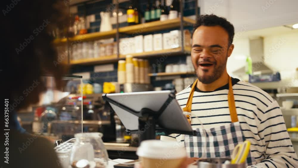 Man with Down Syndrome serving female customer at coffee shop checkout using contactless payment by mobile phone app Man with Down Syndrome serving female customer at coffee shop checkout using contactless payment by mobile phone app