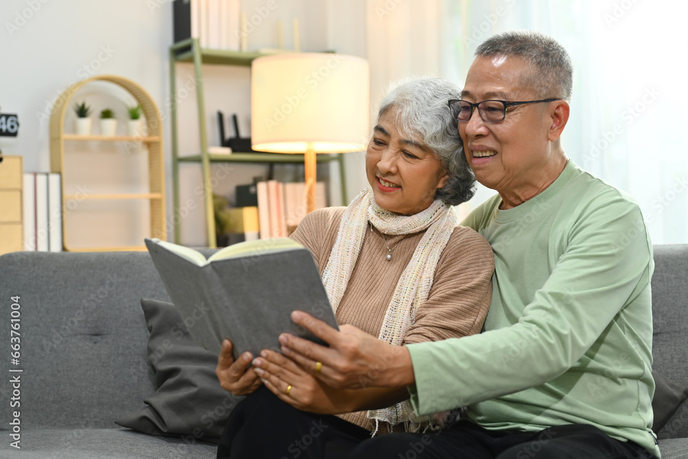 Beautiful senior couple embracing and reading book on sofa while spending time together at home