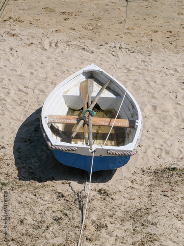 Ein weiß-blaues Ruderboot liegt bei Ebbe auf dem Sandboden des Hafens in Mousehole in Cornwall England photo