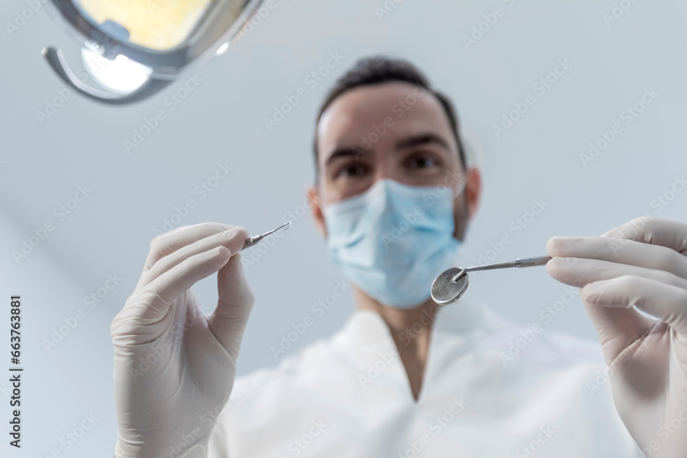 Low angle shot of a male dentist, doing the exam and checking up on oral health of the patient Low angle shot of a male dentist, doing the exam and checking up on oral health of the patient