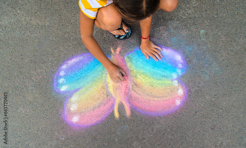 Canvas Print A child draws a butterfly on the asphalt with chalk