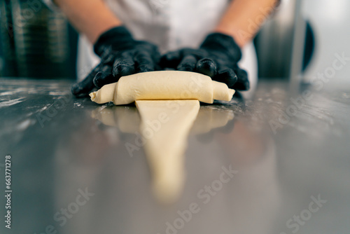 Close-up of the chef's gloved hands shaping and twisting raw dough into shape of croissants for baking photo