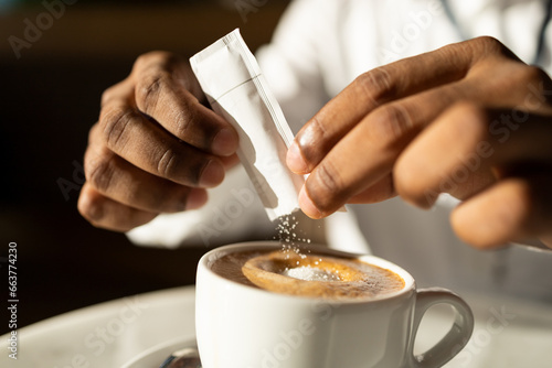 Crop freelancer adding sachet sugar to hot coffee in mug