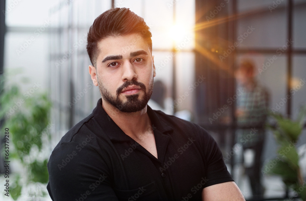 A young handsome businessman in a black shirt stands with his arms crossed.