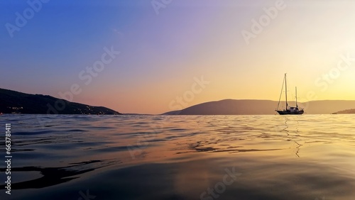 View from the calm sea surface on yacht silhouette against sunset sky and mountains. photo